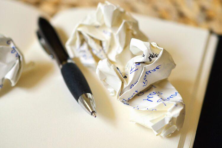 Ballpoint pen and crumpled paper with writing on it atop an open blank journal