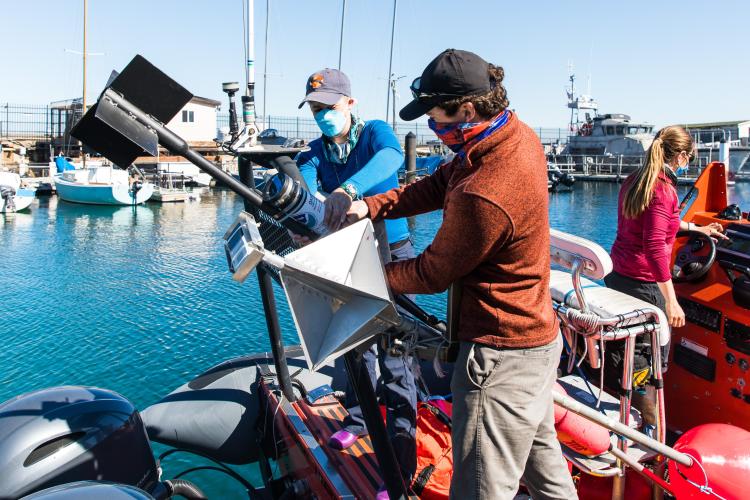 Anne and Jack secure poles to the back of a small boat as they prepare to go out to sea. 