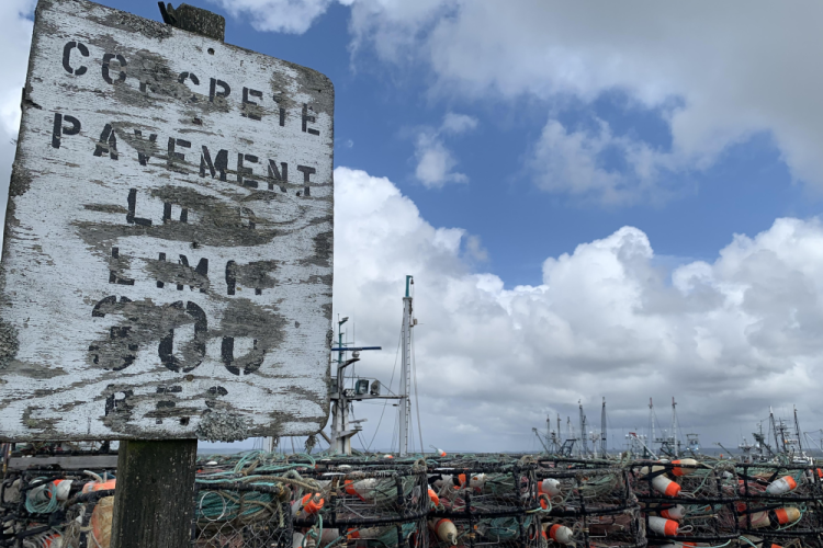 Dungeness crab pots stacked on a pier next to a faded and weathered sign. Credit: NOAA Fisheries