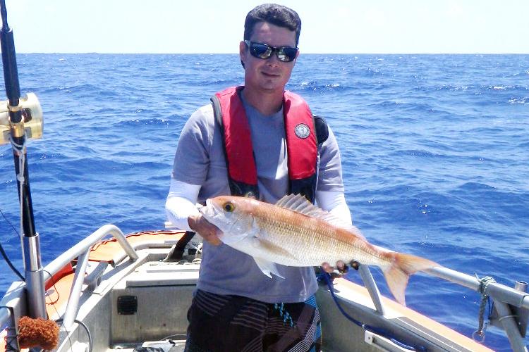 Researcher holding an opakapaka on the deck of a boat.