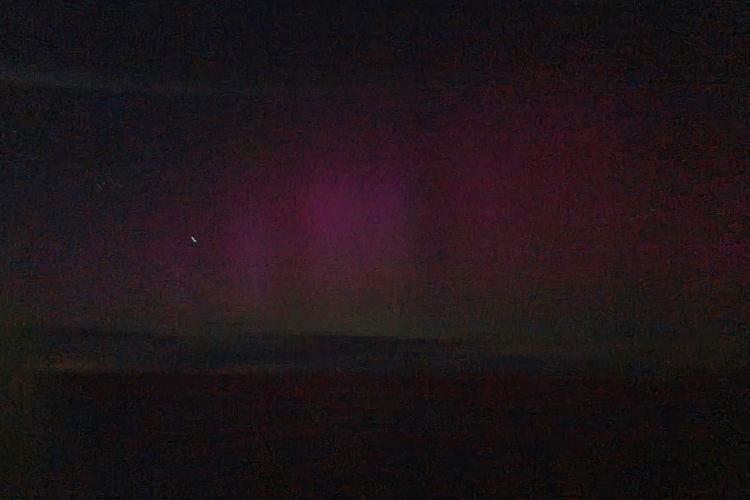 Purple and green streaks across the dark night sky over the water at night.