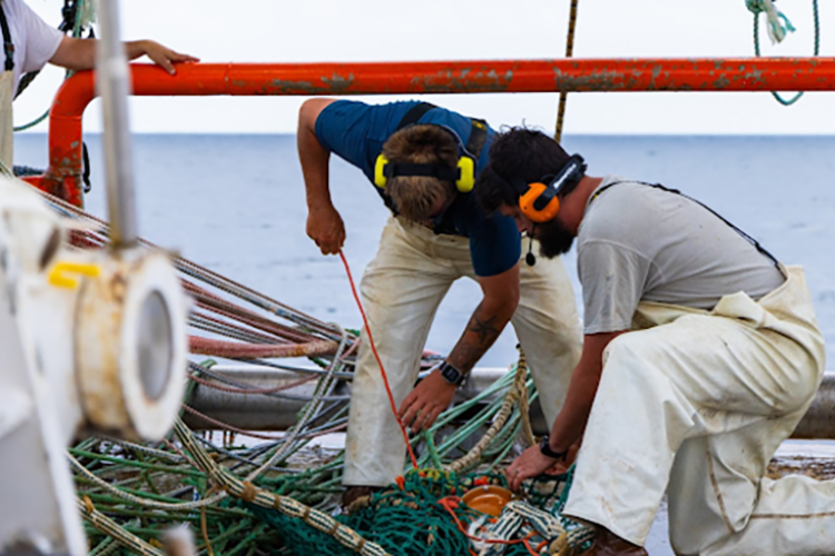 2 men stitch measurement equipment to the net. Both are wearing microphones and headsets.