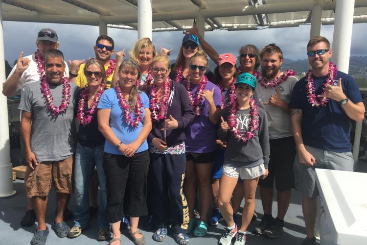 A group of people wearing plumeria leis standing on a ship deck. 