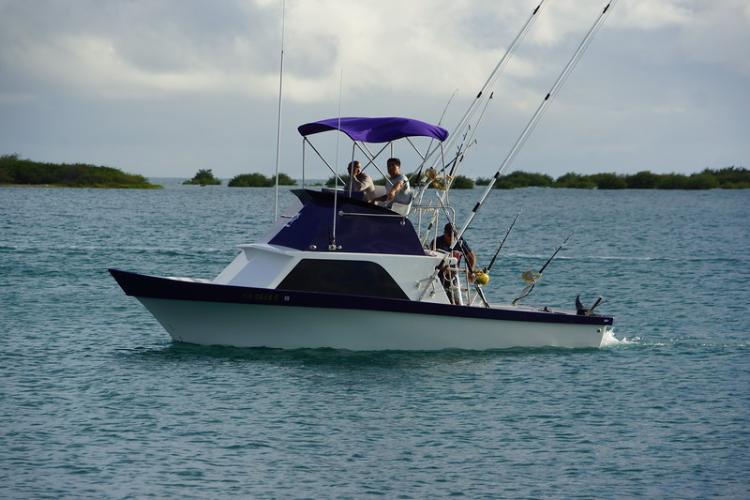 A small fishing vessel with many poles, on the water with small islets in the background. 
