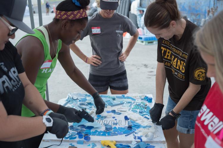 People with gloves and nametags sort pieces of marine plastic onto a NOAA template on a table. 