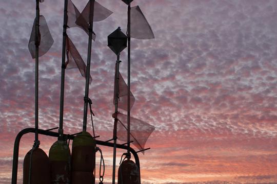 all fishing gear buoys onboard a vessel are silhouetted against textured sky and colored sunset