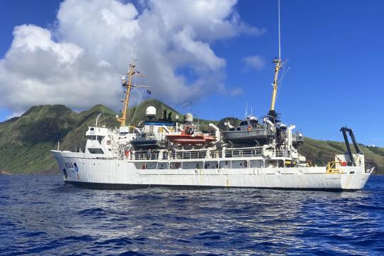 NOAA ship Rainier floats with an island in the background.