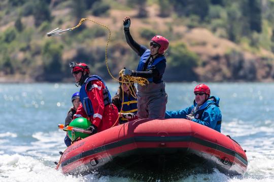 Kathi George aboard an inflatable boat tossing a hook into the water.