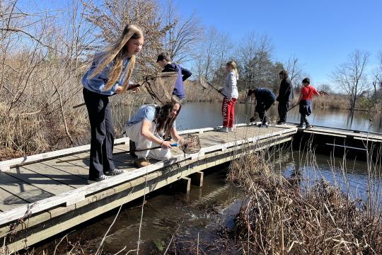 Students stand on a dock, holding nets they are using to explore the wetland.