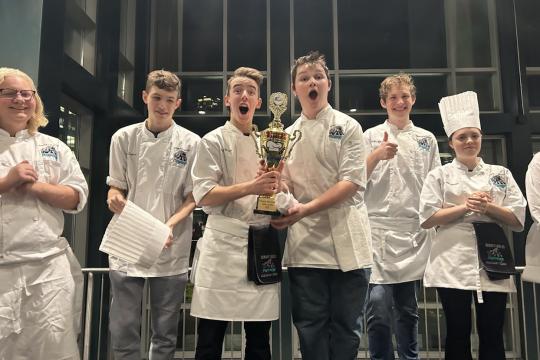 smiling group of young people in chefs outfits holding a trophy 