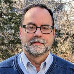 Dan Voorhis, blue sweater, dark framed glasses and beard.