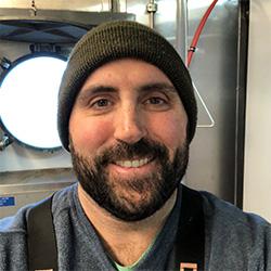 Portrait of scientist with green hat and beard with round boat window in background