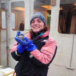 Leah Jones holding sample while in foul weather gear and wearing blue gloves. 