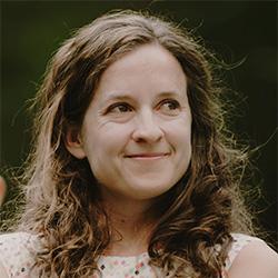 Scientist with curly brown hair smiling and looking into the distance.