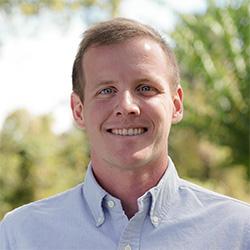 Scientist wearing a button down shirt with greenery in background