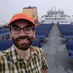 A man in a baseball hat on a ship smiles at the camera.