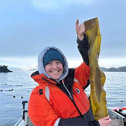 Scienist wearing orange coat holding kelp on a boat. 