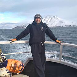 Scientist on boat with snowy mountains in background. 