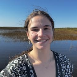 A smiling, young, brunette woman with marshland in the background.