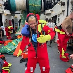Woman putting on a read gumby suite on the deck of a research vessel