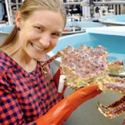 Smiling woman with checker shirt holding up a crab