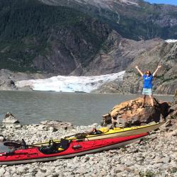 Cathy Tide standing on a rock near kayaks and a glacier