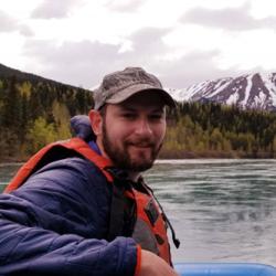 Portrait of man wearing hat and blue coat on a boat with green hills and mountain in background