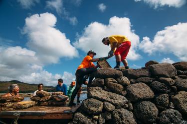 Seven community members wide through shallow water to move and stack rocks for pond structure restoration. 