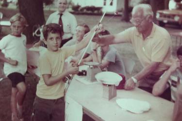 A young boy gives a fishing rod to an older man across a table. 