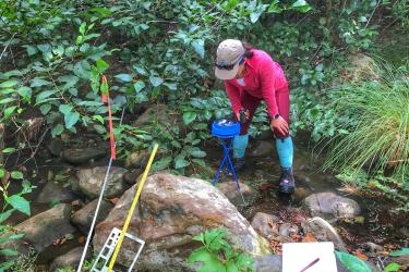 Woman standing in a stream examining a scientific device 