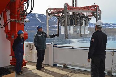 Threee people on a deck of a ship are deploying equipment over the side into the ocean.