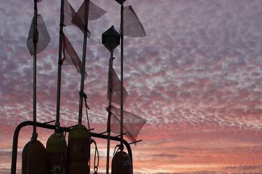 all fishing gear buoys onboard a vessel are silhouetted against textured sky and colored sunset