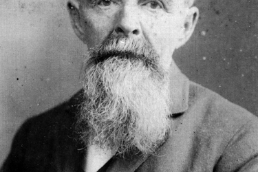 Head and shoulders view of older man with beard wearing a suit coat. 