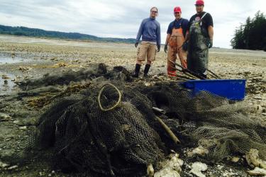 Blair Paul and two colleagues stand in front of derelict nets prior following a beach clean up. 