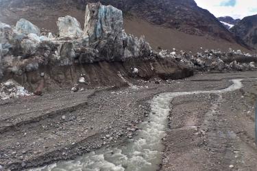 arctic landscape of a glacier in the background and rocky earth cut by a gray-colored stream of whitewater in the foreground