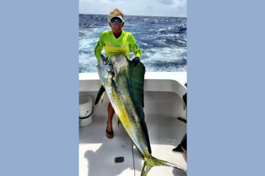 Woman holds caught mahi mahi aboard boat with water in the background