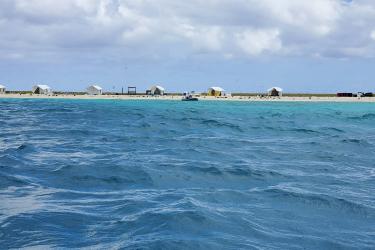 Six temporary white tents setup along the beach with an inflatable boat resting on the shoreline. This photo was taken from a small boat after the temporary field camp was setup at the beginning of the field season in May 2022.