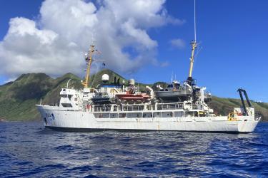 NOAA ship Rainier floats with an island in the background.