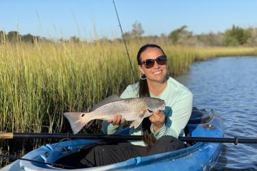 Woman holds a red drum while sitting in a blue kayak on the water