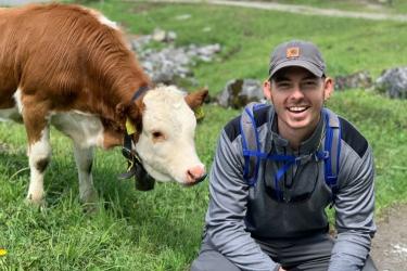 Michael Bradley crouching next to a cow that is brown and white 