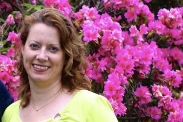 A woman smiles in front of a bush with bright pink flowers 
