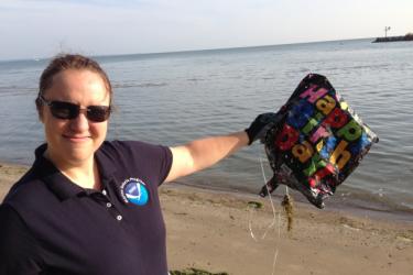A NOAA employee on a beach holding up a deflated Mylar balloon that says Happy Birthday on it.
