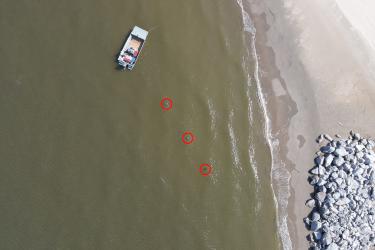 An aerial photograph showing a boat and 3 small toy turtles circled in red in the water.