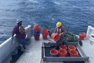 two crew members stand on the back deck of a ship, organizing an array of orange baskets
