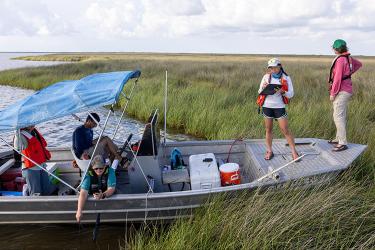 Five people on a boat near a wetland