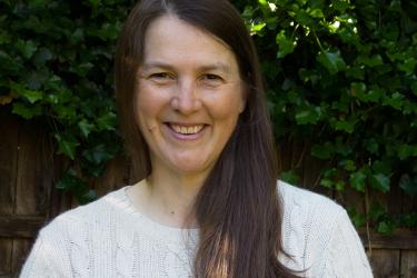 Portrait of scientist with brunette hair and white sweater against background with bushes and a fence