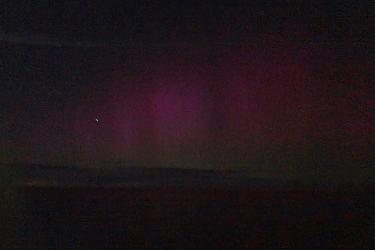  Purple and green streaks across the dark night sky over the water at night.