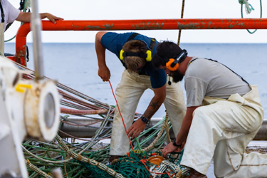 2 men stitch measurement equipment to the net. Both are wearing microphones and headsets.