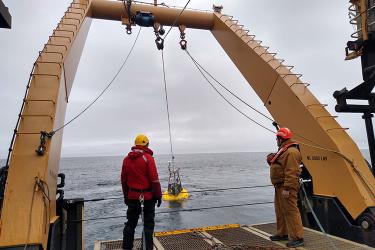 Scientist on a ship watching scientific equipment being deployed in the ocean.