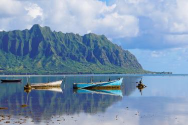 Three small, bare-bones boats moored off a mountainous island coastline
